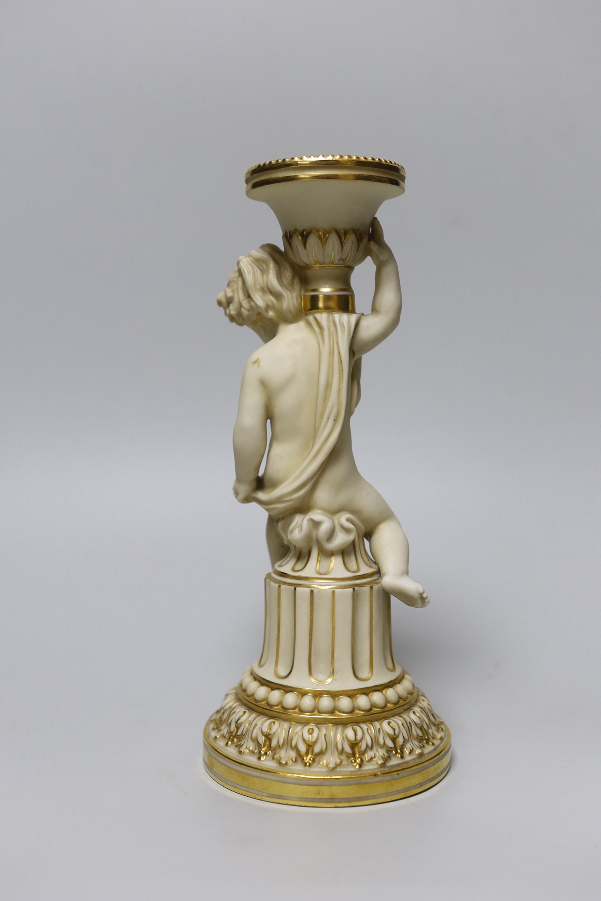 A rare Minton candlestick figure of a cherub seated on part of a column, holding a sonce on it's shoulder, decorated in ivory and gilt, puce MINTONS mark Made for Phillips, with Oxford Street address. 24cm